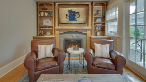 Cozy leather chairs surrounding a small table with a fireplace in the background and decorative shelves.