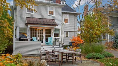 Gray house with a covered porch, surrounded by autumn foliage and an outdoor dining set.