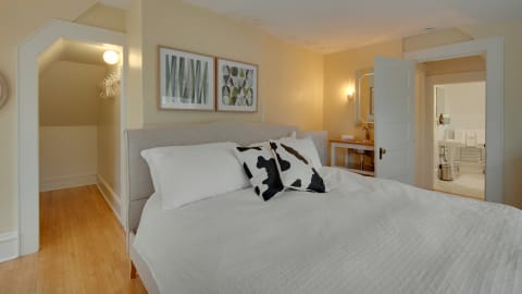 Cozy bedroom featuring a comfortable bed with white linens and decorative pillows, leading to a bathroom.