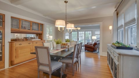 A stylish dining room with a long table, striped chairs, and elegant lighting, filled with natural light.