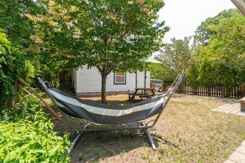 Hammock under a flowering tree in a backyard garden with a picnic table and umbrella.