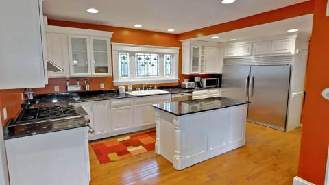 Modern kitchen with orange walls, white cabinetry, and granite countertops.