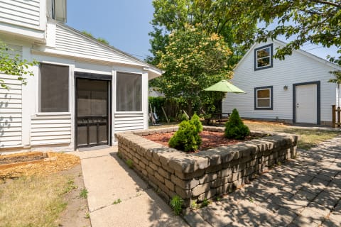 A peaceful backyard with a screened door, stone flower bed, and a green umbrella over a picnic table.
