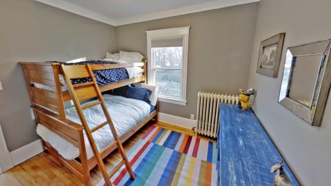A charming bunk room featuring a wooden bunk bed, striped rug, and a colorful dresser.