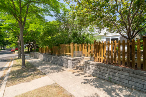A residential street with a wooden picket fence, trees, and a sidewalk in a tranquil neighborhood.