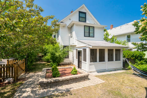 A Victorian-style white house with a screened porch, surrounded by mature trees and a landscaped yard.