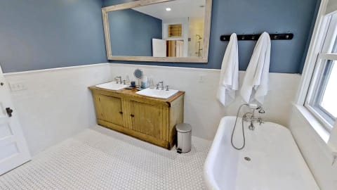 A vintage-style bathroom featuring a wooden vanity with double sinks, a freestanding tub, and a serene blue wall.