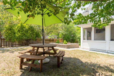 Wooden picnic table with benches under a large green umbrella in a garden setting.