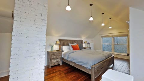 A modern rustic bedroom featuring a wooden bed, soft gray bedding, and warm lighting with a white brick wall.