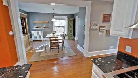 Open-concept kitchen and dining area showcasing hardwood floors, white cabinets, and a pop of orange wall color.