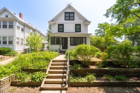 A two-and-a-half-story white house with a landscaped garden and steps leading to the porch.