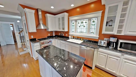 A modern kitchen with black granite countertops, white cabinets, stainless steel appliances, and vibrant orange walls.
