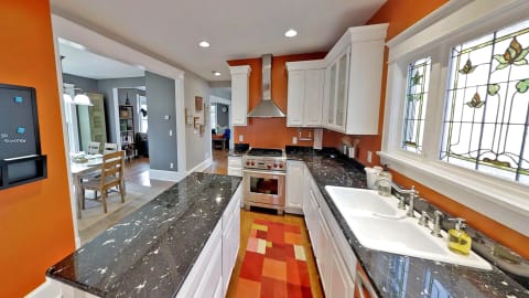A spacious modern kitchen with granite countertops, stainless appliances, and orange walls, brightened by stained glass windows.