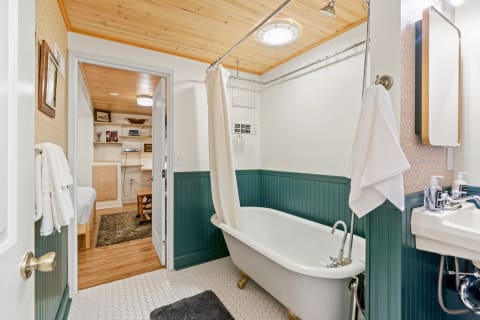 A vintage bathroom with a clawfoot bathtub, green wainscoting, and a wooden ceiling.