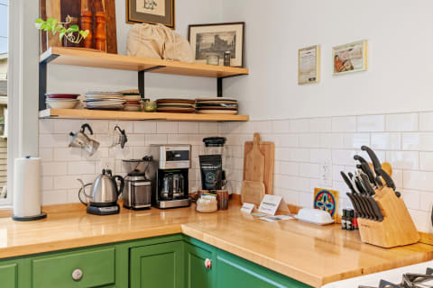 A cozy kitchen corner featuring green cabinets, open shelves with plates, and various kitchen appliances on a wooden countertop.