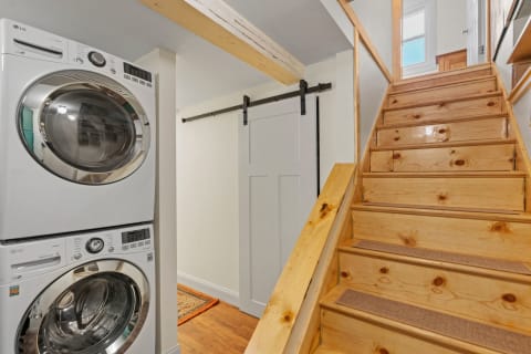 Laundry room featuring a stacked washer and dryer with wooden stairs leading up.