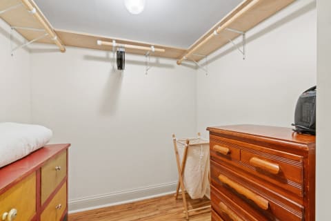A tidy closet featuring a wooden chest of drawers, a laundry hamper, and a clothing rod with hangers.