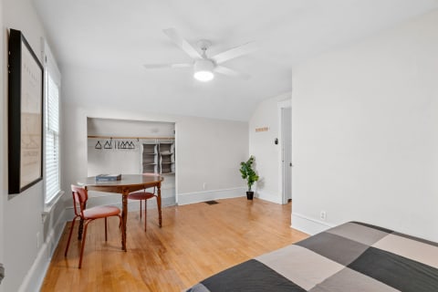 Bright bedroom featuring hardwood floors, a workspace with a table and chairs, and an organized closet.