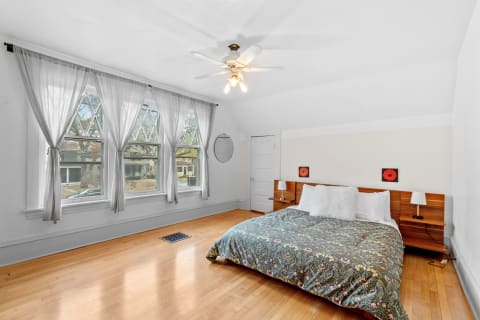Bright bedroom with hardwood floors, large windows, stylish curtains, and a cozy bed.