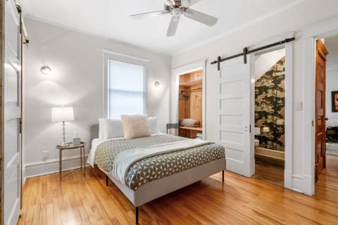 A stylish bedroom with hardwood floors, a geometric-patterned bed, and a barn door leading to another space.