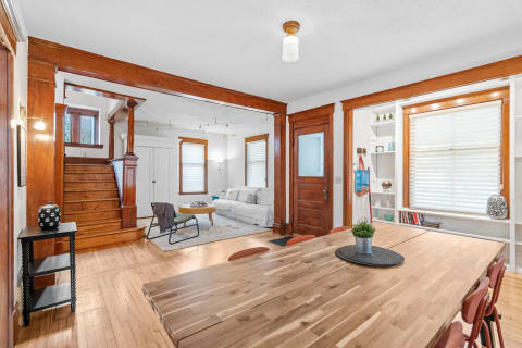 A warm and inviting dining area featuring a wooden table with chairs, leading into a cozy living room with a white sofa.
