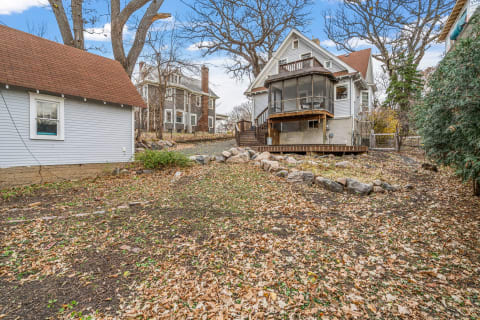 A serene residential backyard with fallen leaves, a stone path, and historic homes in the background.