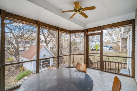 A screened porch featuring a round table, wooden chairs, and views of the neighborhood through mesh screens.