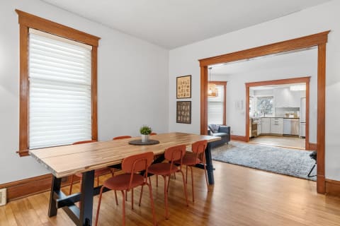 Dining area with wooden table and orange chairs, leading to a living space and kitchen.