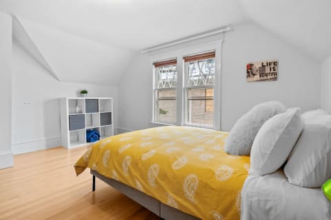 Bright yellow bedding in an attic bedroom with wooden flooring and natural light from two windows.