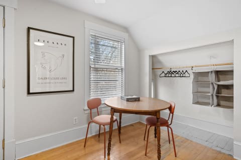 A cozy dining nook with a round wooden table, pink chairs, and a Picasso print on the wall, illuminated by natural light.