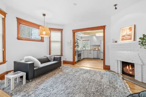 A living room with a sofa, fireplace, and an open kitchen area, highlighting a warm atmosphere with natural light.