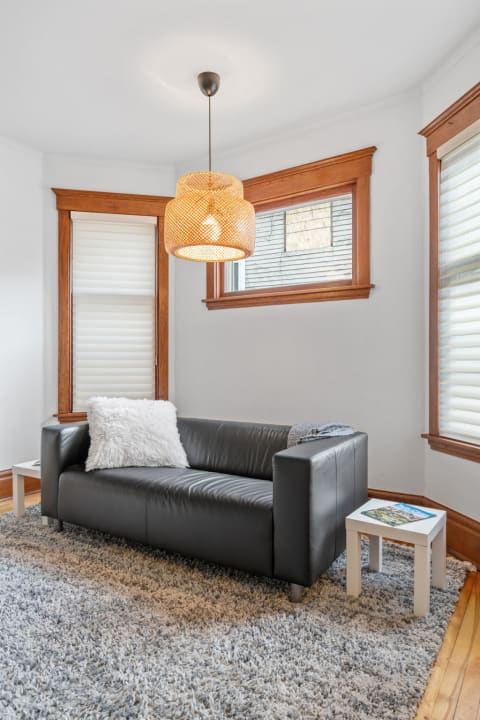 A cozy reading nook with a black leather couch and woven pendant light.