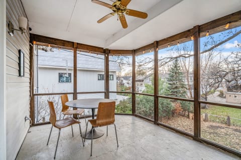 Screened porch with a round table and wooden chairs, offering views of a landscaped neighborhood.
