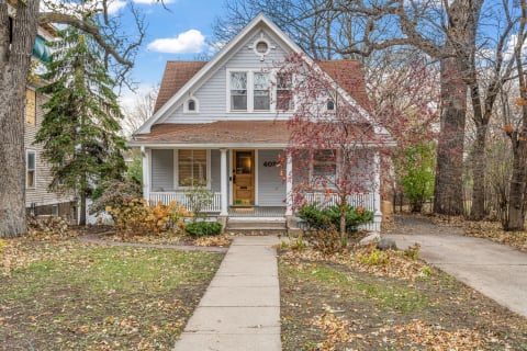 A two-story house with a front porch surrounded by trees and autumn leaves.