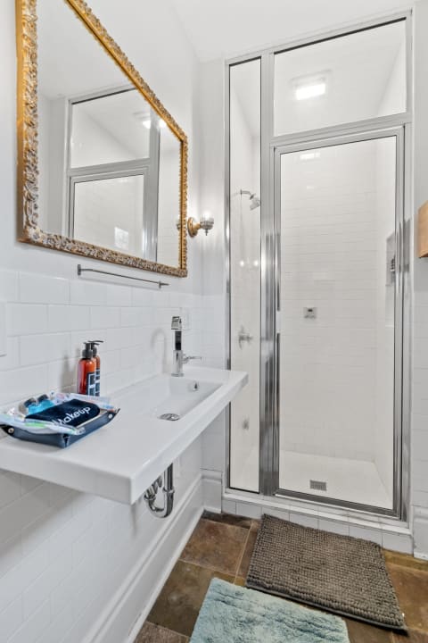 Modern bathroom with white tiles, stylish sink, walk-in shower, and ornate mirror.