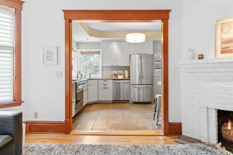 View of a modern kitchen through a wooden archway, featuring stainless steel appliances and bright natural light.