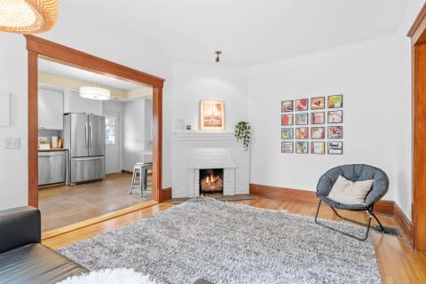 Cozy living room with a fireplace, gray shag rug, gallery wall, and view of the kitchen.