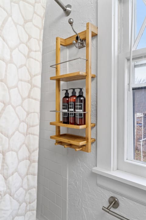 Bamboo shelves in a shower displaying shampoo, conditioner, and body wash bottles against a textured wall.