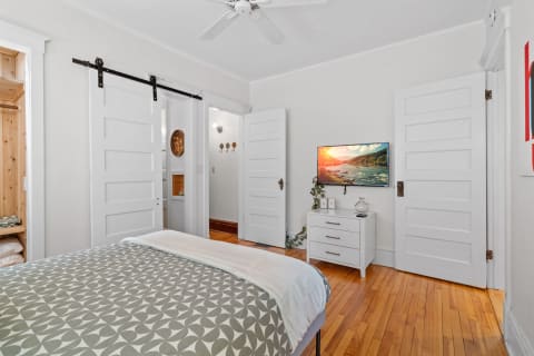 A cozy bedroom with hardwood floors, stylish bed, flat-screen TV, and barn door leading to a closet.