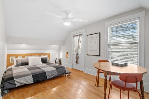Cozy bedroom with hardwood floors, a stylish bed, and a dining table by the window.