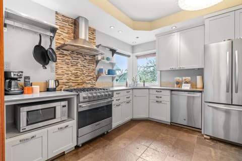 Spacious kitchen with stainless steel appliances, gray cabinets, and natural light from windows.