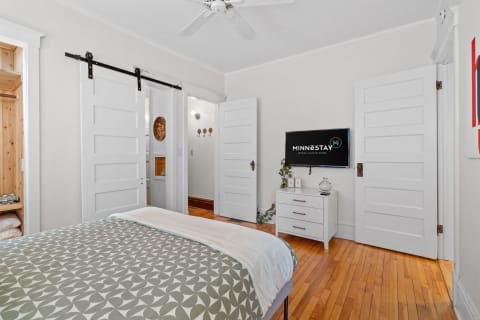 A stylish bedroom with hardwood floors, a geometric-patterned bedspread, a flat-screen TV, and sliding barn doors.