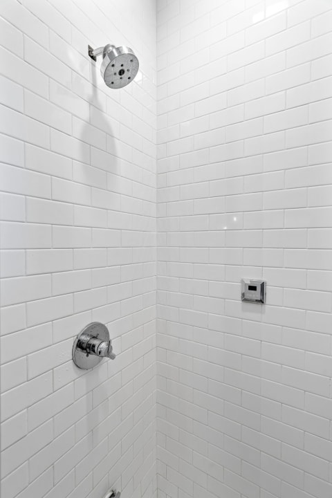 A beautifully tiled shower with chrome fixtures and rainfall showerhead in a minimalist design.