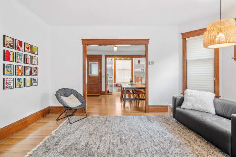 A stylish living room with a charcoal sofa, artwork on the wall, and an archway leading to a dining area.