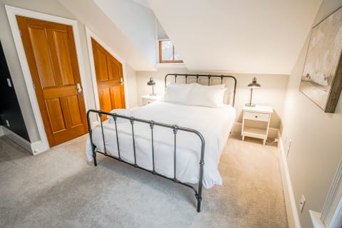 Cozy attic bedroom with an iron bed, white linens, and wooden doors.
