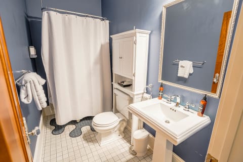 A cozy bathroom featuring blue walls, a white shower curtain, classic fixtures, and neatly arranged towels.