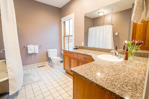 Spacious bathroom with granite countertops, warm wood cabinets, and fresh tulips.