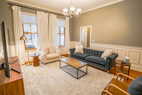 A stylish living room with a dark gray tufted sofa, a light armchair, and warm lighting.