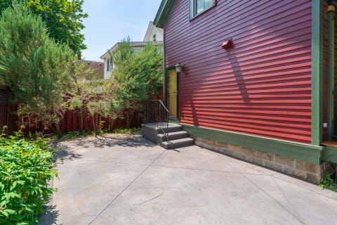 Side view of a home with red siding, steps leading to a private entrance, and green plants around.