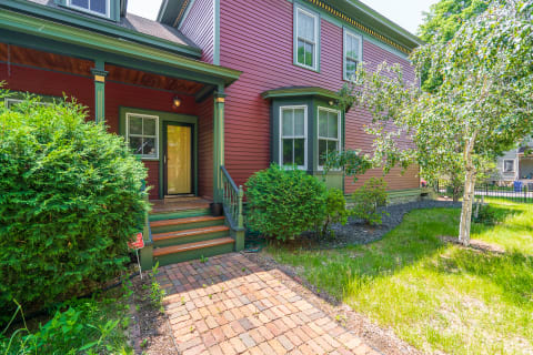 Victorian house with burgundy siding, yellow door, and landscaped front yard.